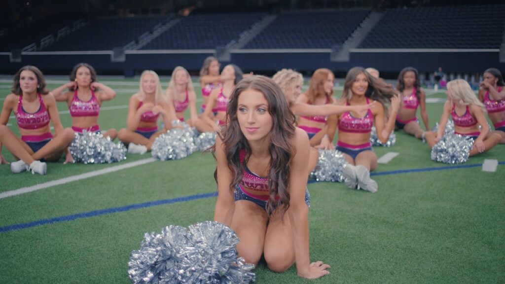 Dallas Cowboys Cheerleaders in pink uniforms warming up with pom poms on the field